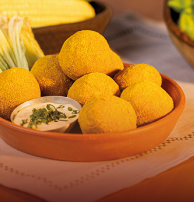 Tigela de barro com bolinhos de chica doida fritos e espigas de milho ao fundo